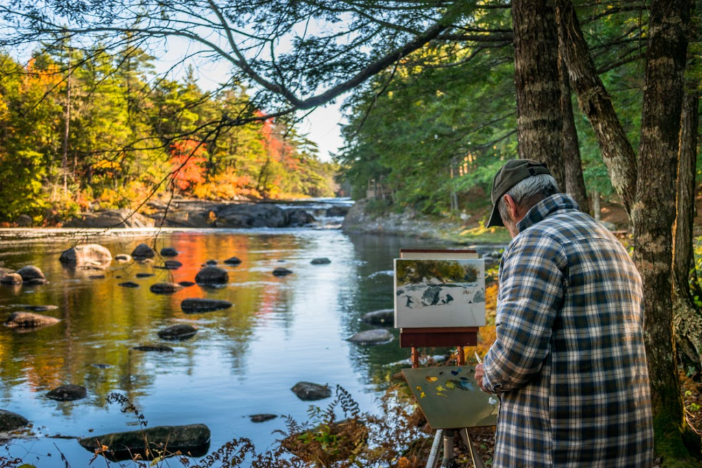 A senior painting scenery outdoors.