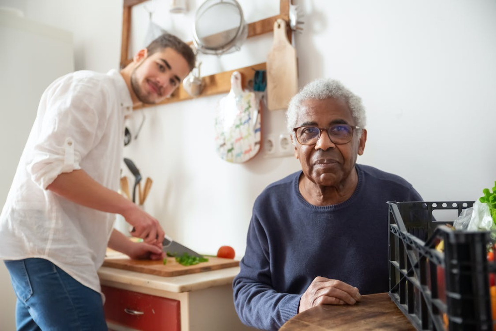 A senior with their caregiver cutting vegetables.