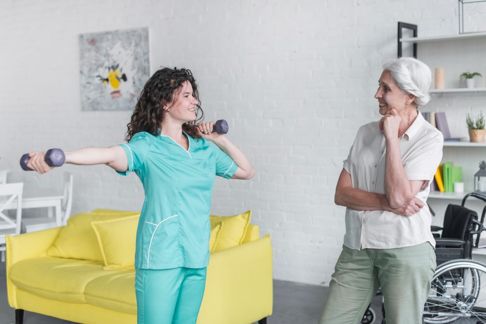 A caregiver teaches a senior gentle exercise in a bright and airy fitness room