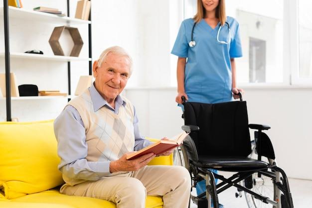 A senior reading a book with a caregiver behind a wheelchair next to them