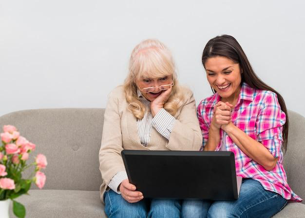 A senior with a young individual watching something on a laptop