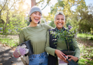 A senior holding a potted plant with a person helping them