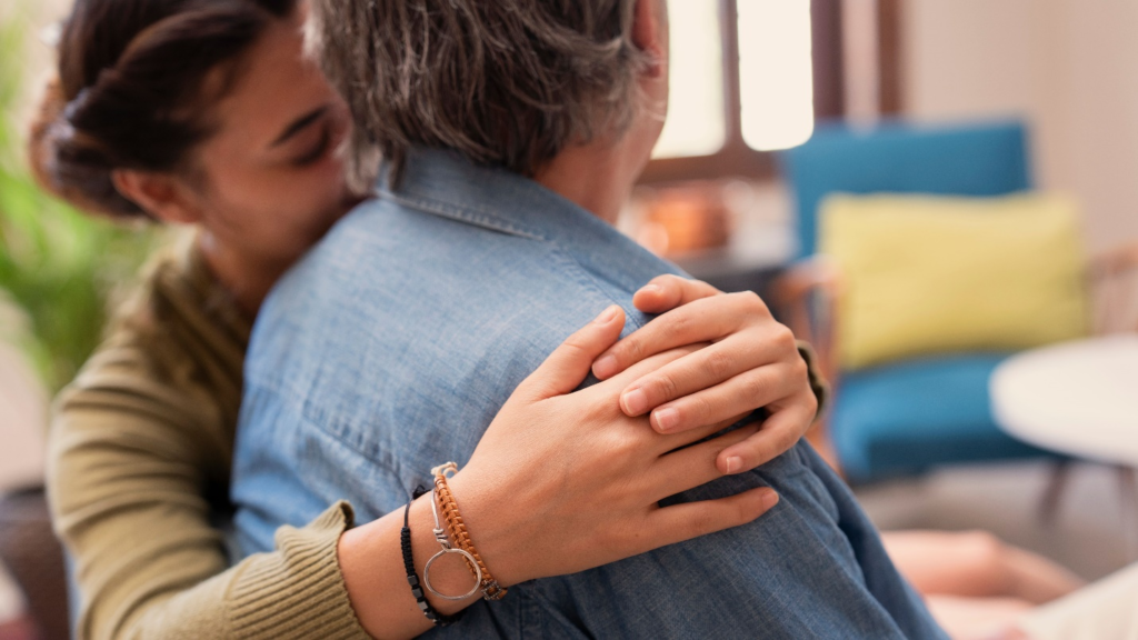 A person wrapping their arms around their senior loved one's shoulder